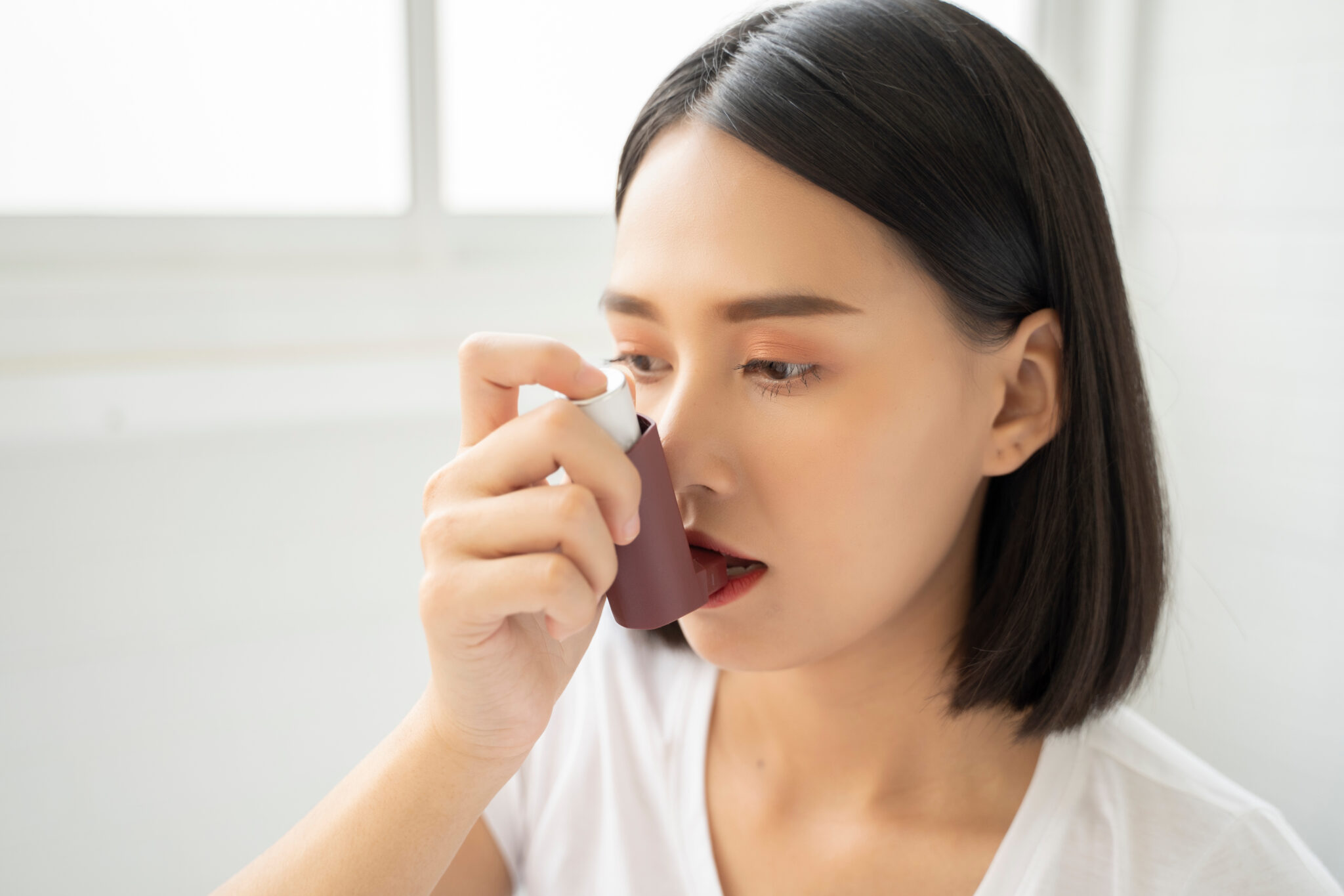 asian woman having asthma using the asthma inhaler for being healthy on her bed in bedroom